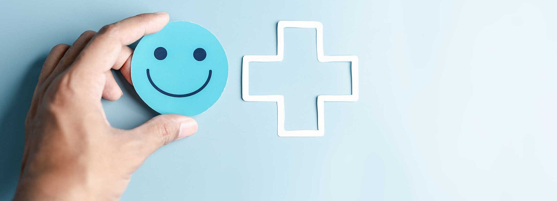 Bild einer Hand, die ein Smiley neben ein medizinisches Kreuz hält.
